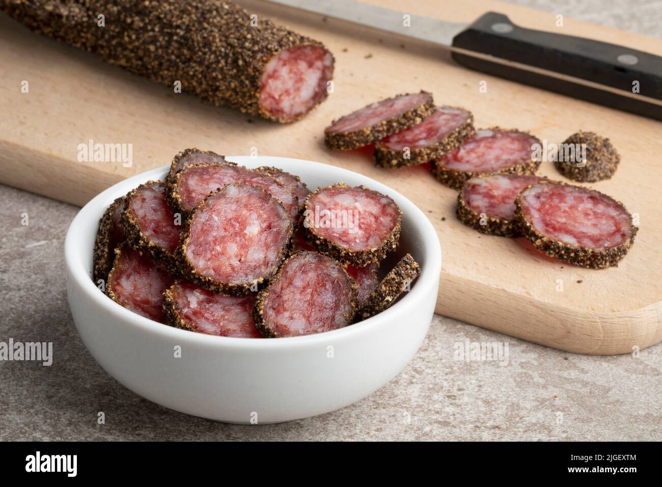 Salsiccia catalana tradizionale, fuet, e fette ricoperte di pepe nero su un tagliere da vicino Foto Stock