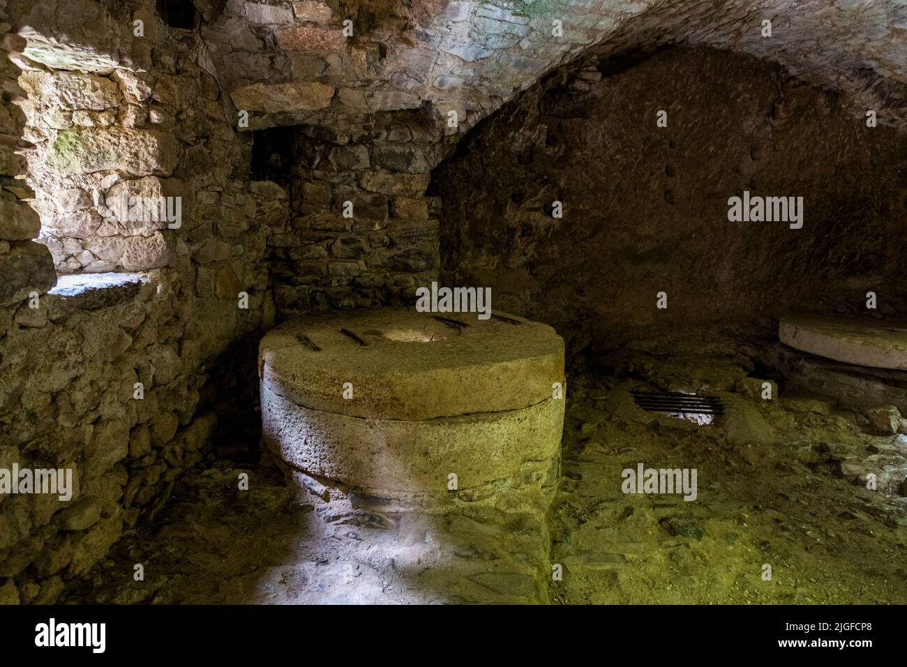 Una vecchia macina si trova all'interno dell'intero a volta dei Moulins de la Foux vicino a Navacelles, Le Vigan, Gard, Francia. Secondo una carta fondazionale, l'origine di questi mulini risale al 1097. Muschio umido copre le pareti di pietra della volta. Foto Stock