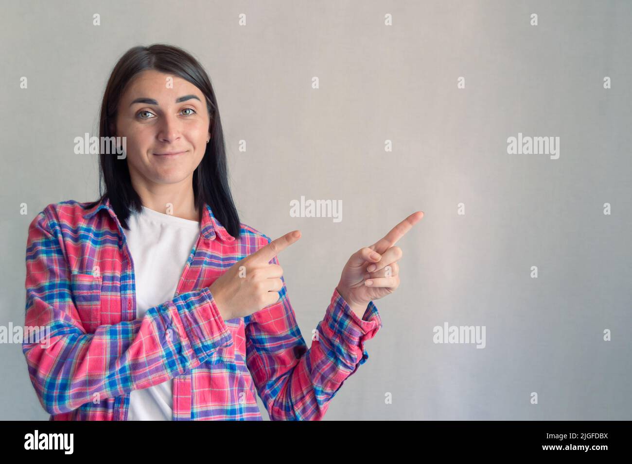 Giovane attraente donna sicura in maglia casual mostrando le dita puntando a qualcosa o spazio di copia vuoto testo offerta area. Sfondo grigio. Por Foto Stock