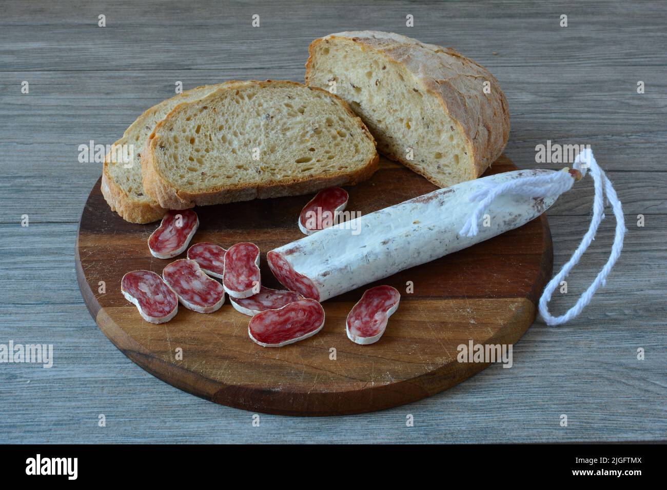 Salsiccia spagnola molto piccante con muffa bianca, tagliata su tagliere di legno scuro, con pane scuro, vista laterale Foto Stock