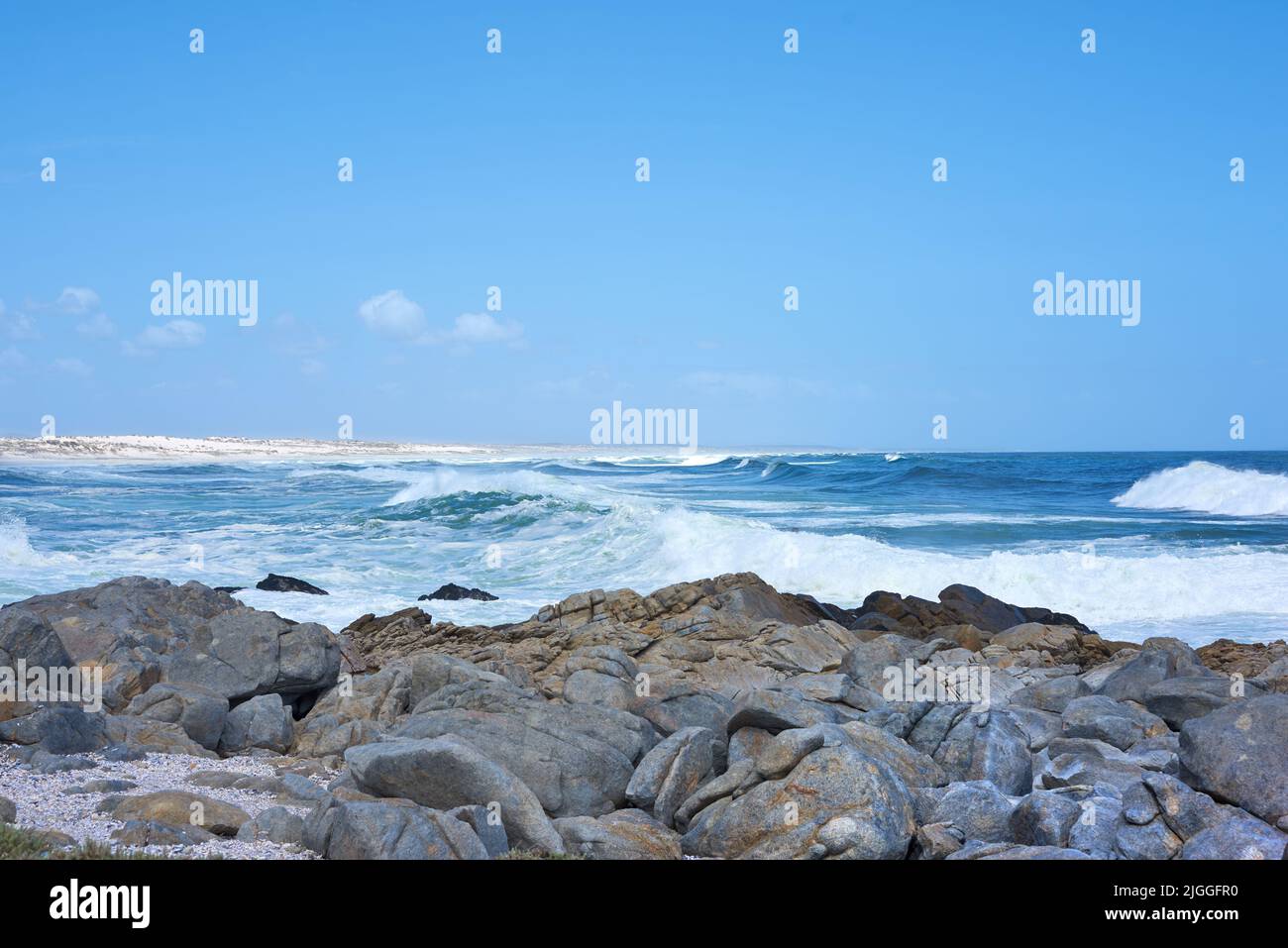 Rocce nell'oceano sotto un cielo blu con spazio copia. Bel paesaggio di onde di spiaggia che si schizzano contro massi o pietre grandi nel mare a un Foto Stock Rocce nell'oceano sotto un cielo blu con spazio copia. Bel paesaggio di onde di spiaggia che si schizzano contro massi o pietre grandi nel mare a un Foto Stock