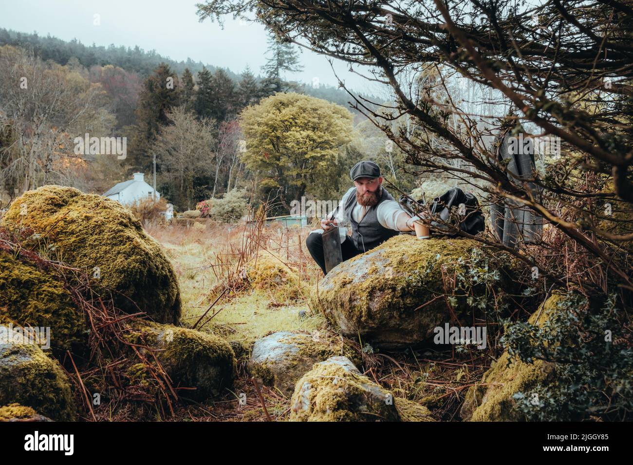 Uomo elegante che raggiunge per una tazza nelle montagne di Wicklow, Irlanda. 1920s tema. Uomo trendy brutale sicuro bearded. Foto Stock