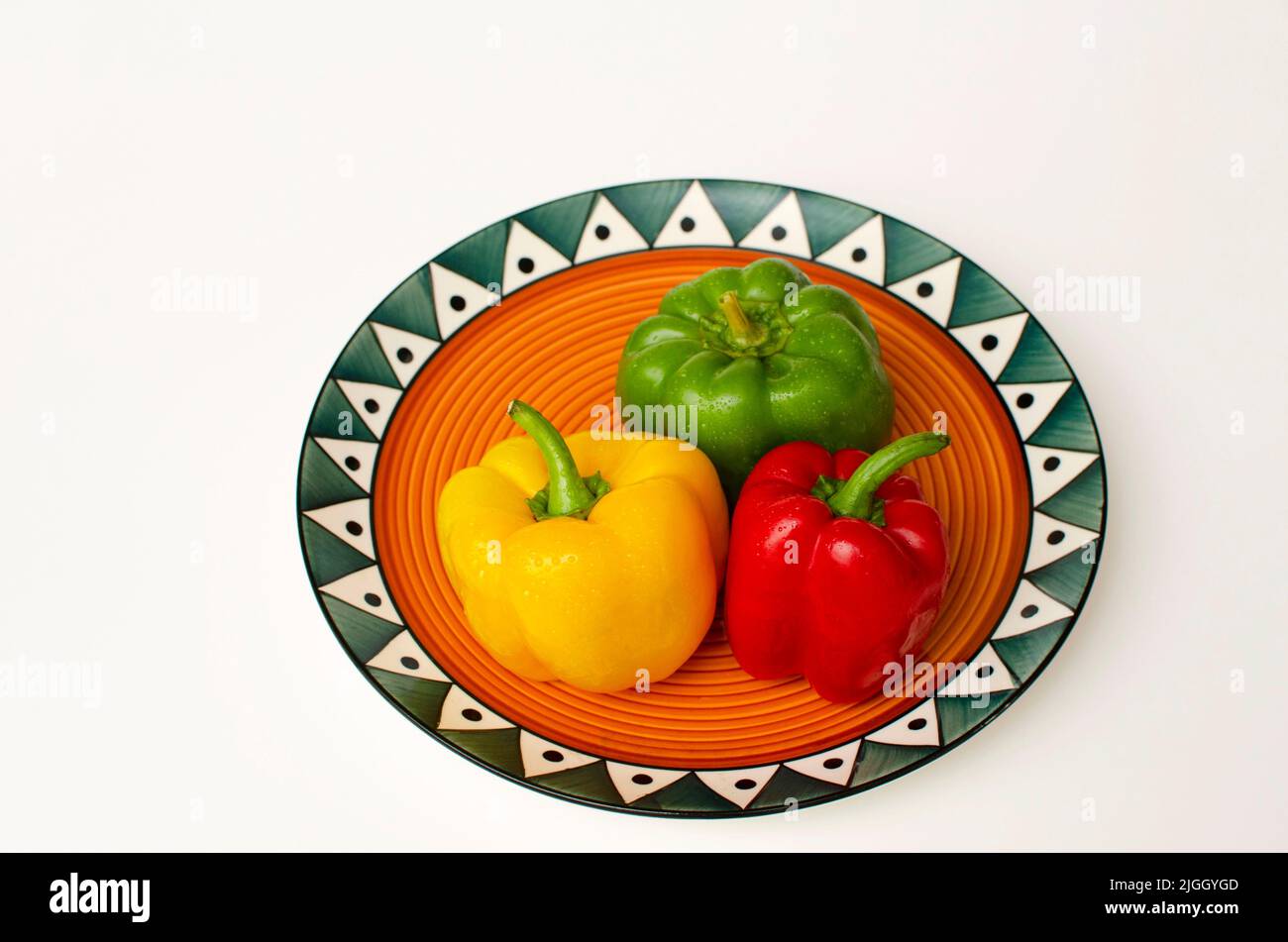 Peperone verde, rosso e giallo fresco in un piatto colorato su sfondo bianco Foto Stock