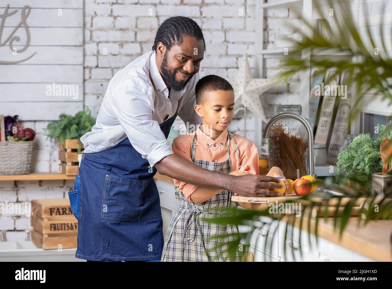 Il padre nero e il bambino che cucinano verdure fresche in cucina a casa. Papà africano e bambino ragazzo che si preparano insieme. Foto Stock