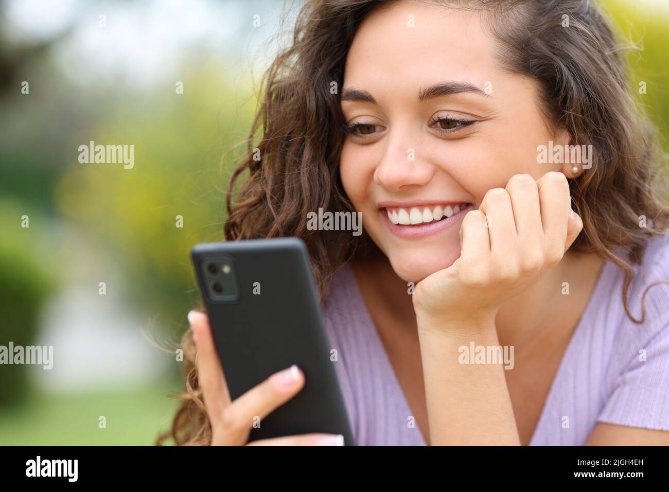Donna felice controllare smartphone sorridendo in un parco Foto Stock