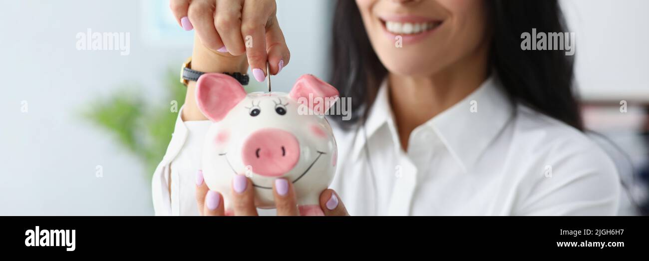 Donna felice che mette le monete in contenitore di piggybank e sorridente Foto Stock