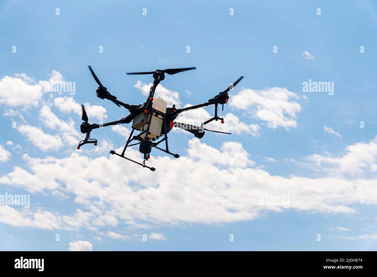 Un drone irroratrice vola su un campo di grano, nel cielo blu con le nuvole. Agricoltura intelligente e coltivazione di precisione. Un drone industriale nel cielo. Foto Stock Un drone irroratrice vola su un campo di grano, nel cielo blu con le nuvole. Agricoltura intelligente e coltivazione di precisione. Un drone industriale nel cielo. Foto Stock