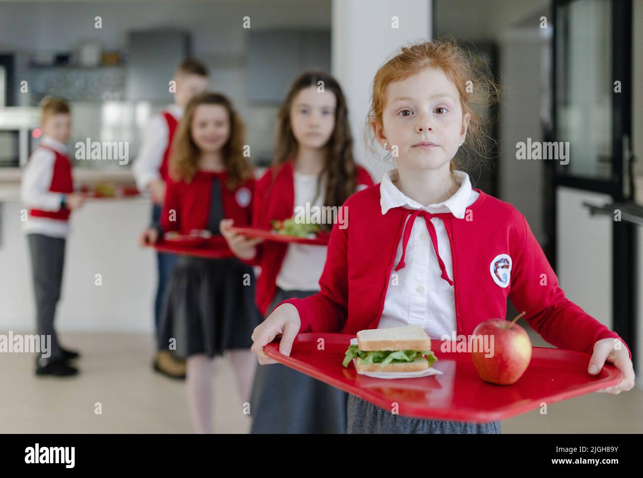 Scolari felici in uniformi che tengono vassoi con pranzo e in coda in mensa scolastica. Foto Stock