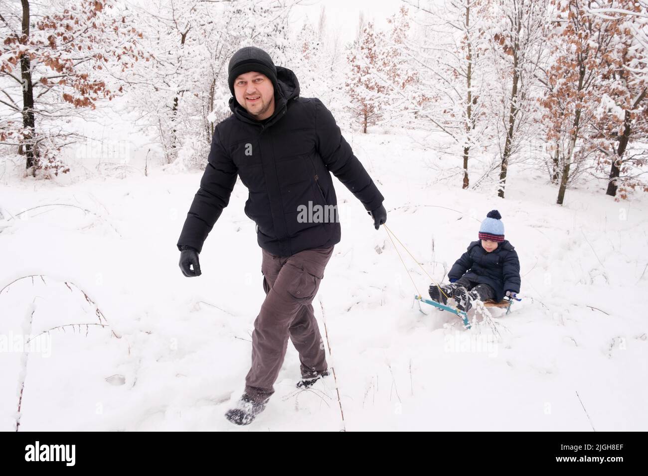 Papà che ha slittato suo figlio in una stazione sciistica in una foresta invernale coperta di neve Foto Stock