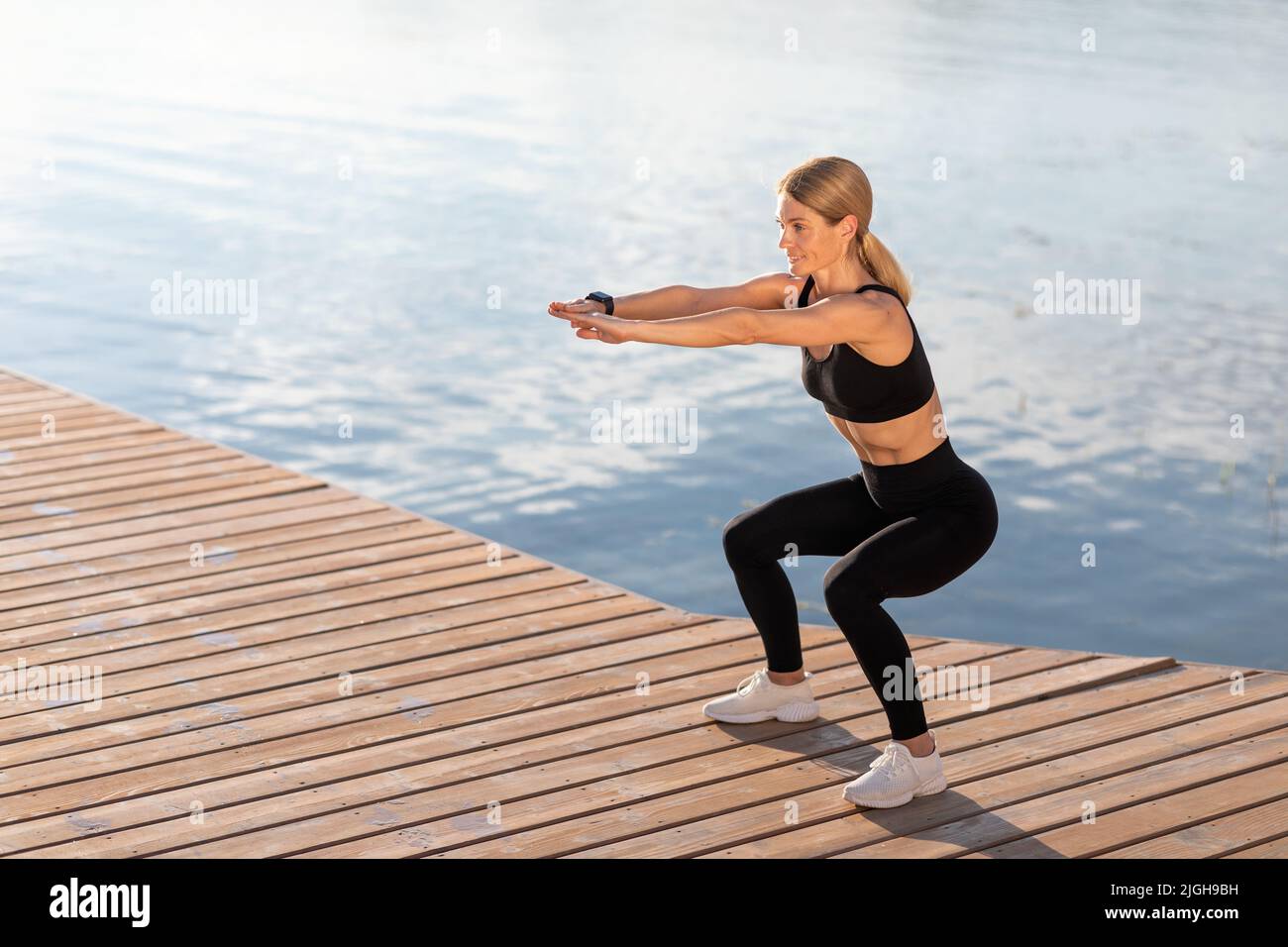 Formazione all'aperto. Sorridendo donna di mezza età facendo squats esercitarsi sul molo, Foto Stock