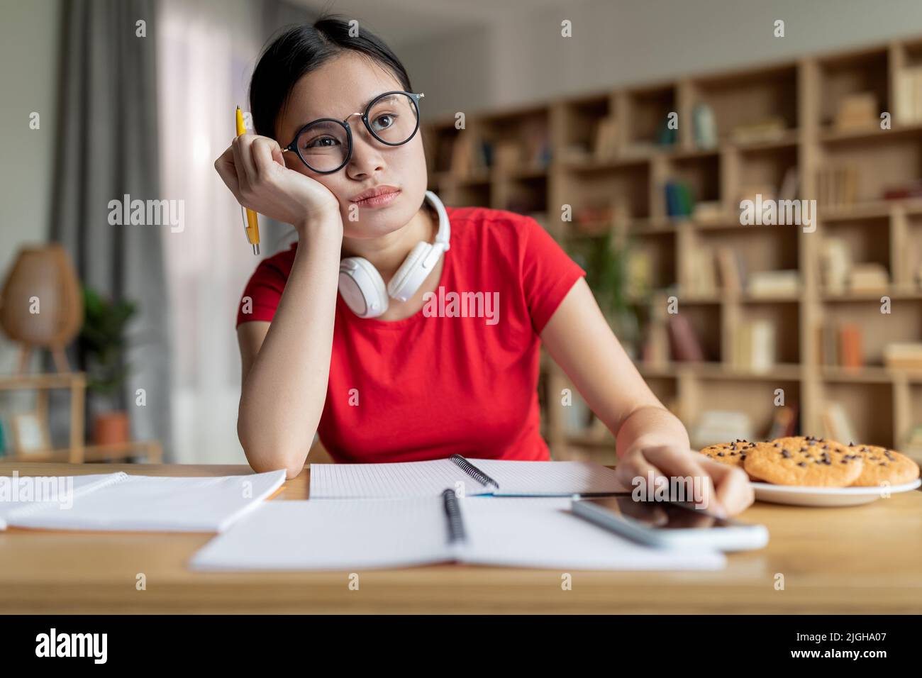 Noiosa ragazza asiatica teenage stanca in occhiali con cuffie studiare a distanza, fare una pausa, riposare Foto Stock