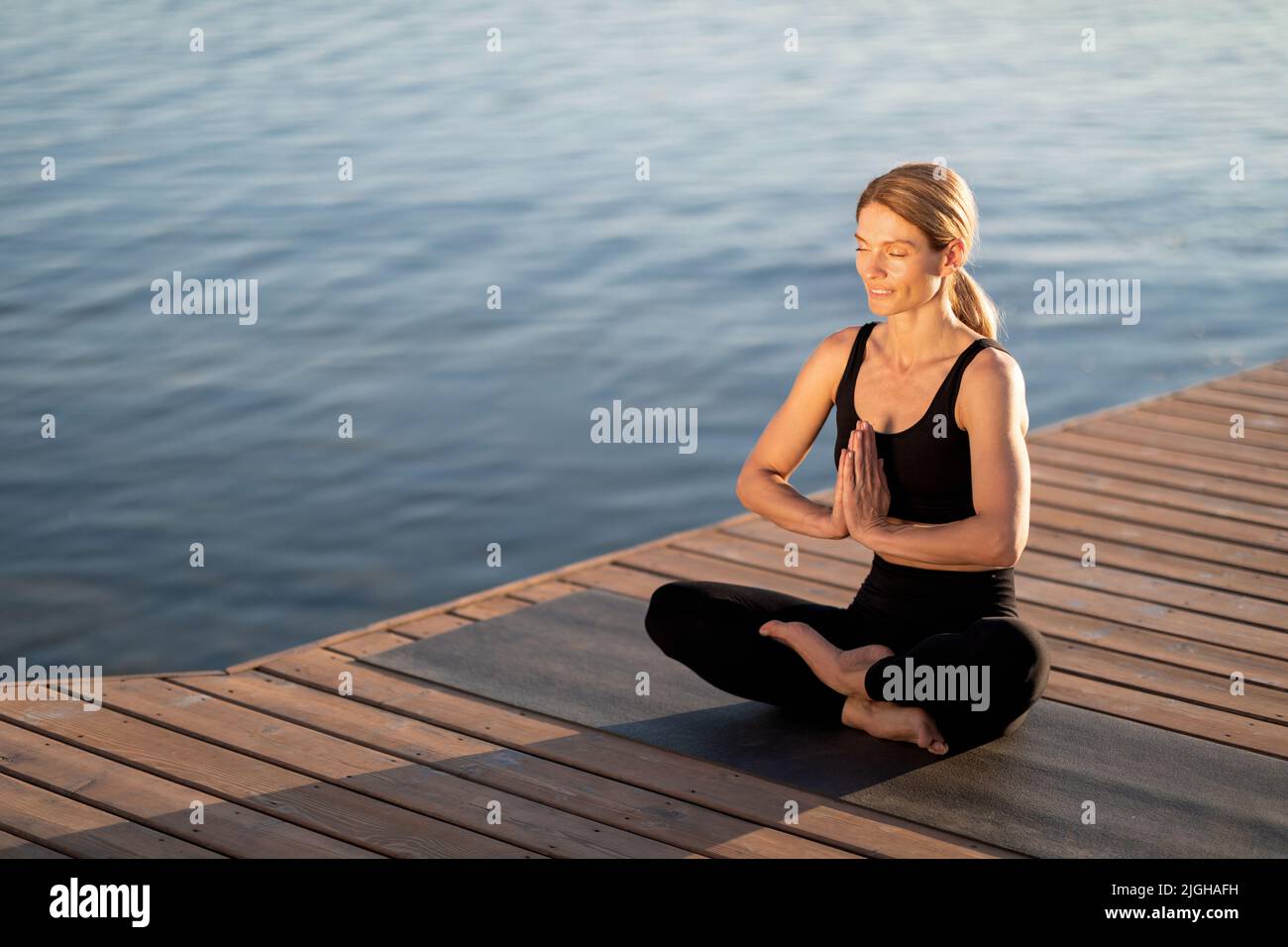 Meditazione del mattino. Calma Donna di mezza età meditating all'aperto su Molo di legno Foto Stock