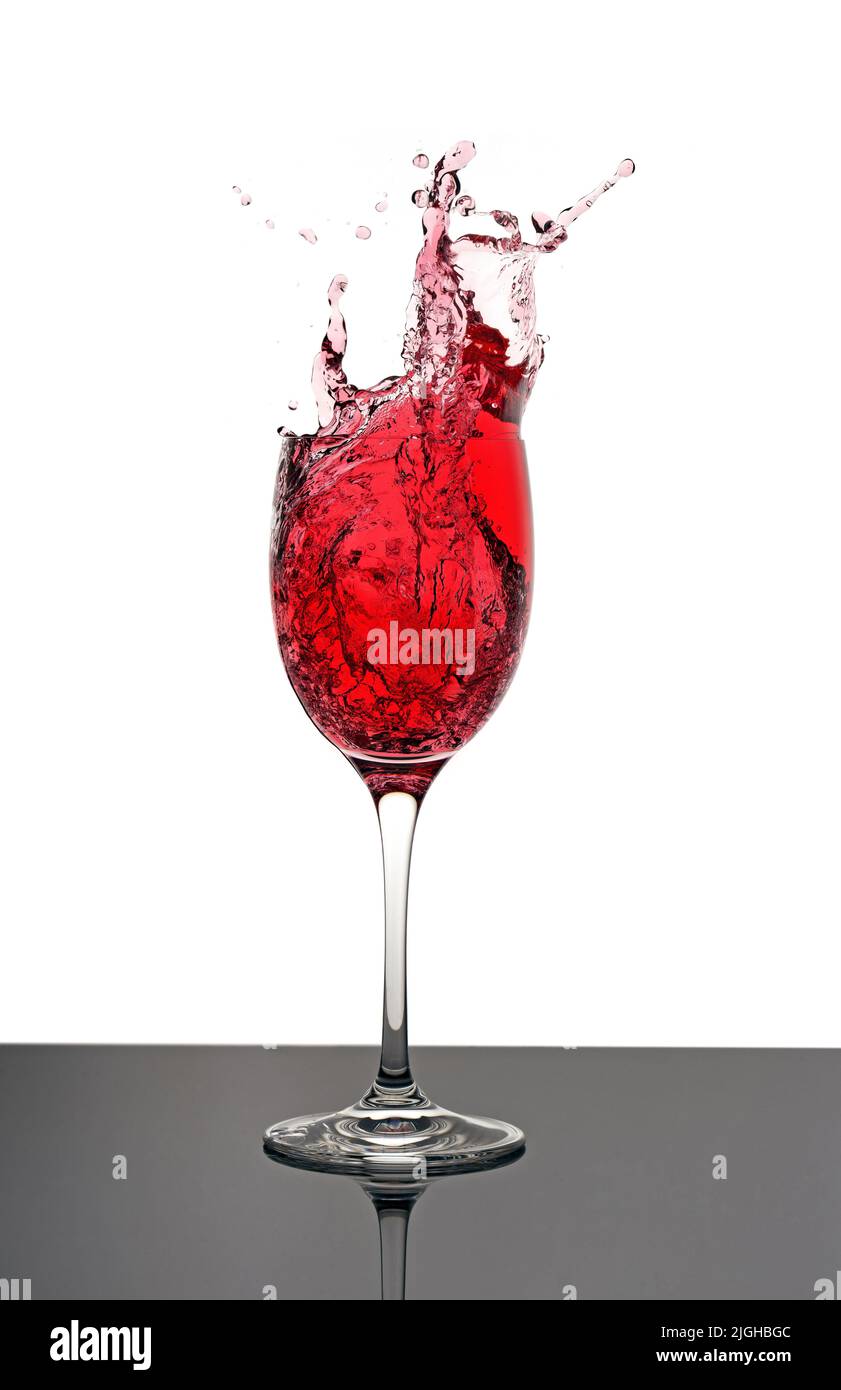 vino rosso che si spacca in un bicchiere di gambo Foto Stock