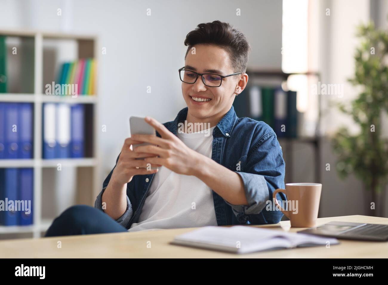 Nuova app. Sorridente giovane uomo d'affari che si rilassa con il laptop sul posto di lavoro in ufficio Foto Stock