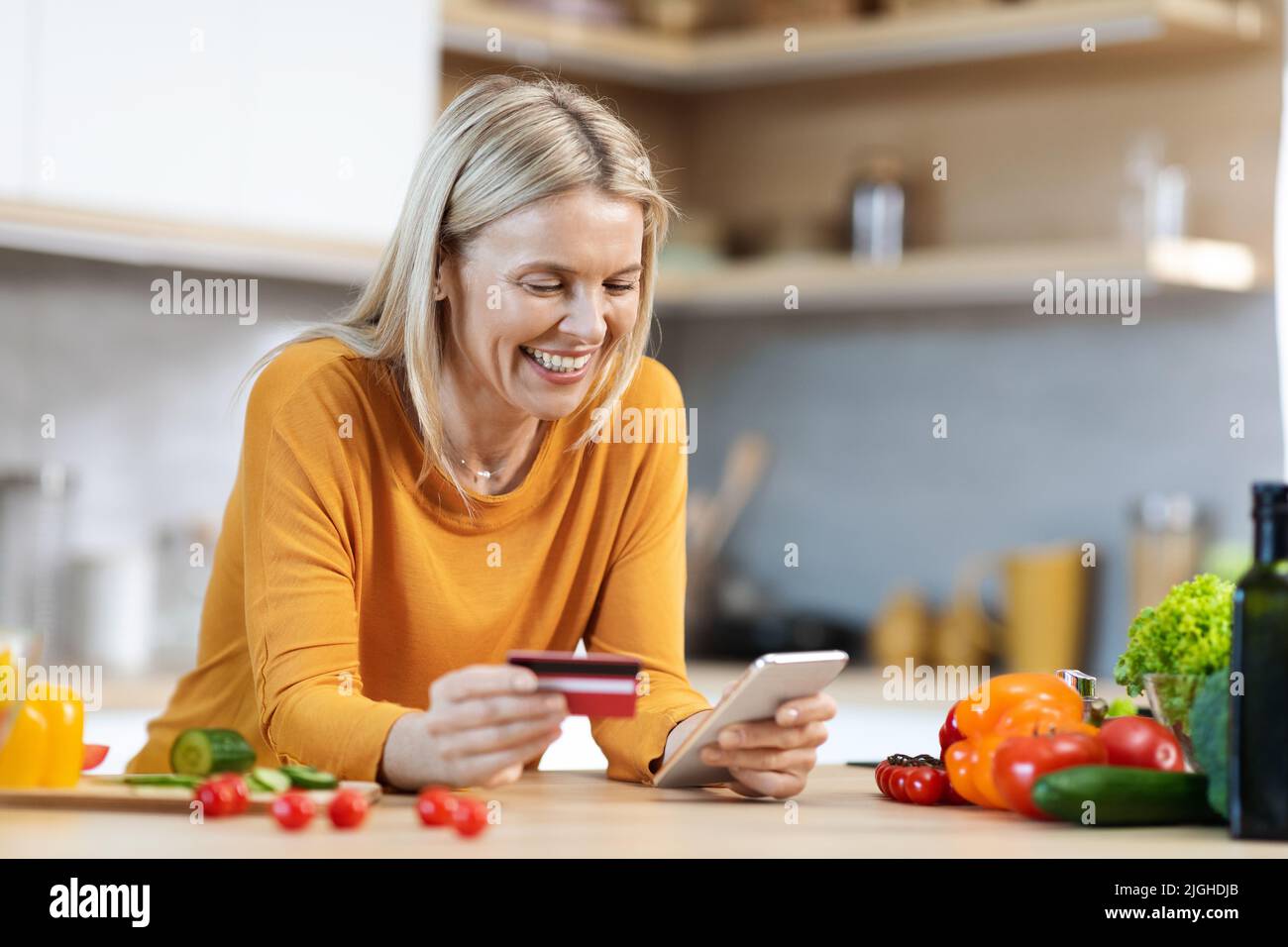 Donna bionda felice che acquista cibo online, utilizzando lo smartphone Foto Stock