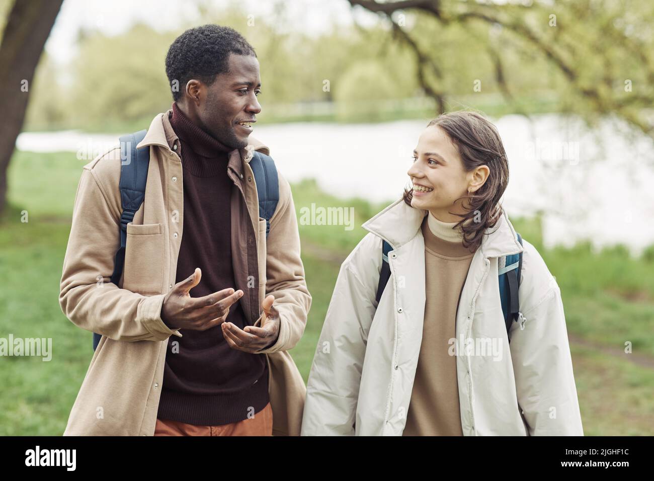 Felice coppia multietnica sorridente durante la conversazione mentre camminano lungo il parco Foto Stock