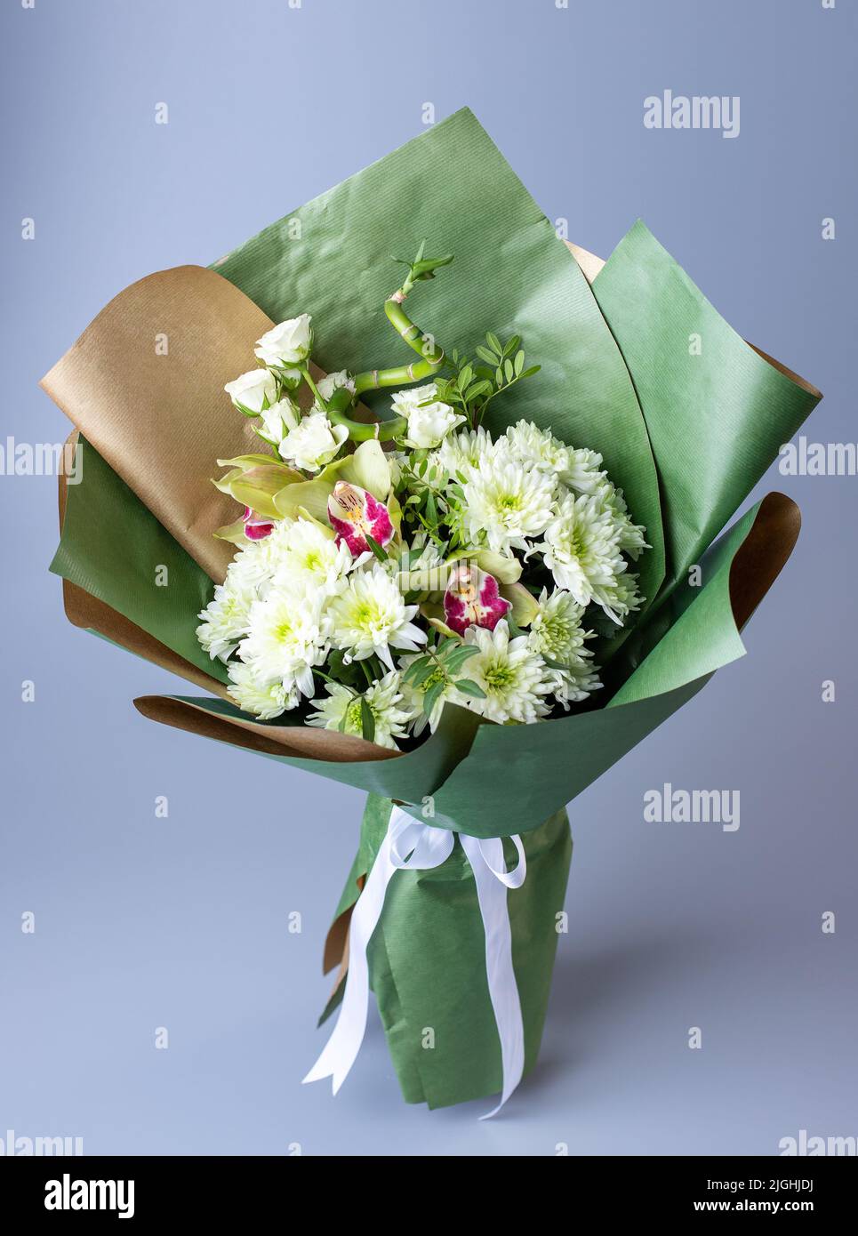 Bouquet originale con crisantemi bianchi, eustoma e rami verdi. Bouquet di fiori avvolti in kraft e carta verde con ribo bianco Foto Stock