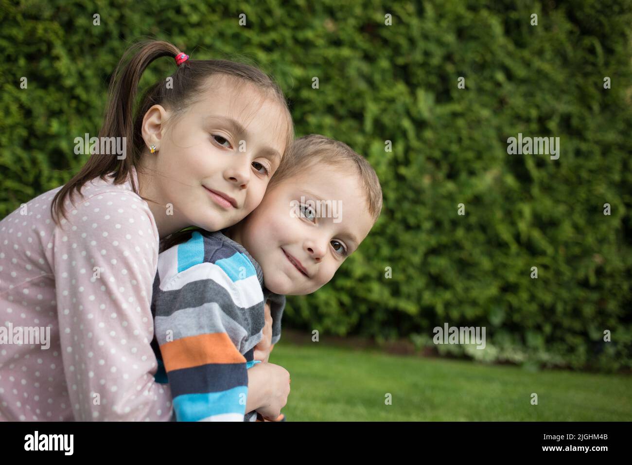 Ritratto di sorridente fratello minore e sorella maggiore, seduti insieme nel parco, abbracciato. Felice vita bambini. Rapporti amichevoli tra Foto Stock