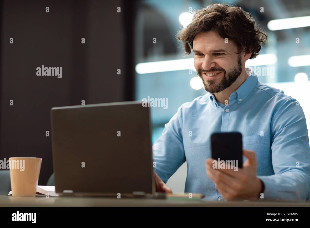 Happy dipendente azienda maschile maturo controllare il cellulare, utilizzando il portatile, lavorare online in ufficio, spazio copia Foto Stock