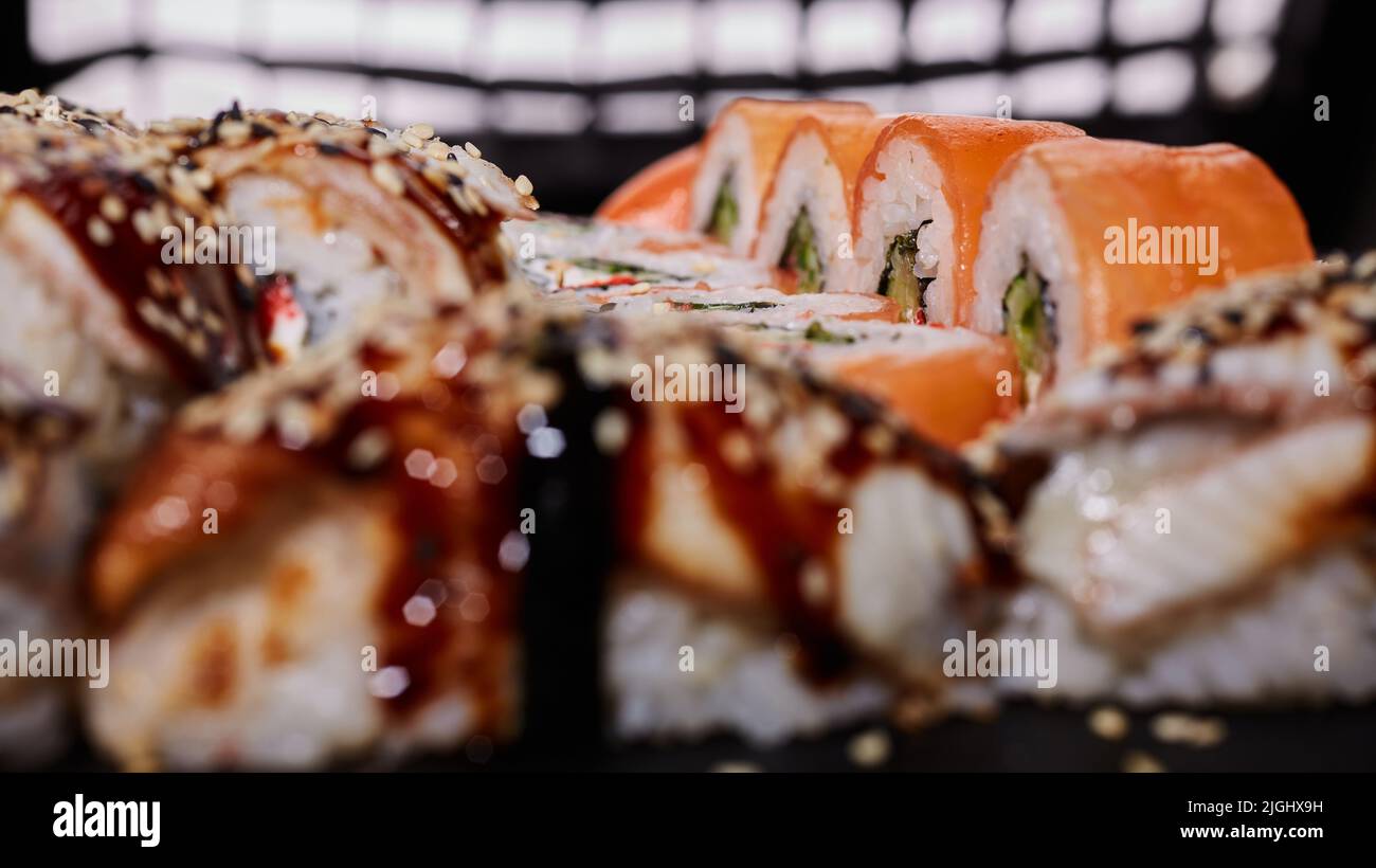 Primo piano macro shot di un rotolo di Philadelphia con formaggio cremoso, salmone, cetriolo e caviale si trova tra gli altri rotoli. Messa a fuoco selettiva. Fronte sfocato Foto Stock