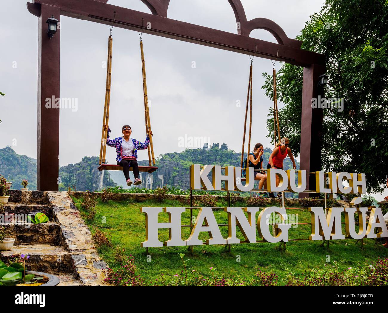 Swing set con 2 posti a sedere sufficientemente larghi per due persone all'ingresso della grotta di Mua a Ninh Binh, VN. Turisti che si divertono. Foto Stock