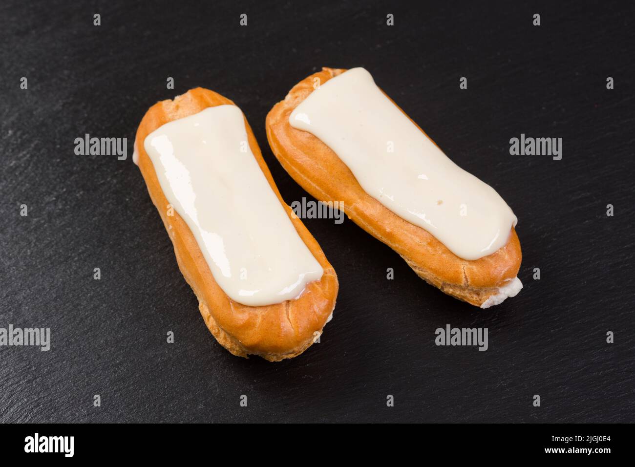 Eclairs con crema bianca isolata su sfondo nero. Foto Stock