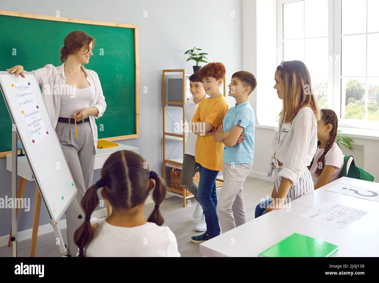 L'insegnante della scuola felice usa la lavagna bianca della classe mentre fa la presentazione per i bambini Foto Stock