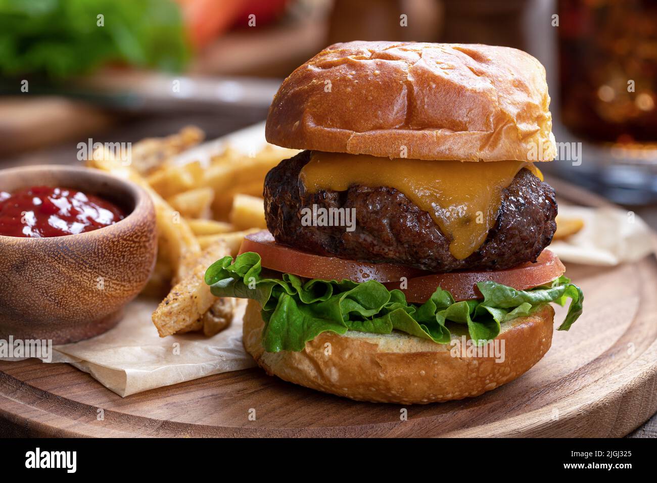 Cheeseburger con lattuga e pomodoro su panna tostata con patatine fritte e ketchup su piatto di legno Foto Stock