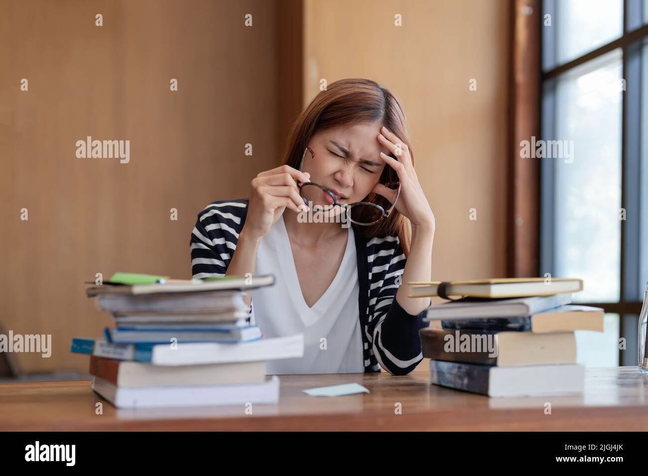 Studente asiatico seduto con un gruppo di mani mal di testa leggere l'esame finale nella biblioteca universitaria. Foto Stock