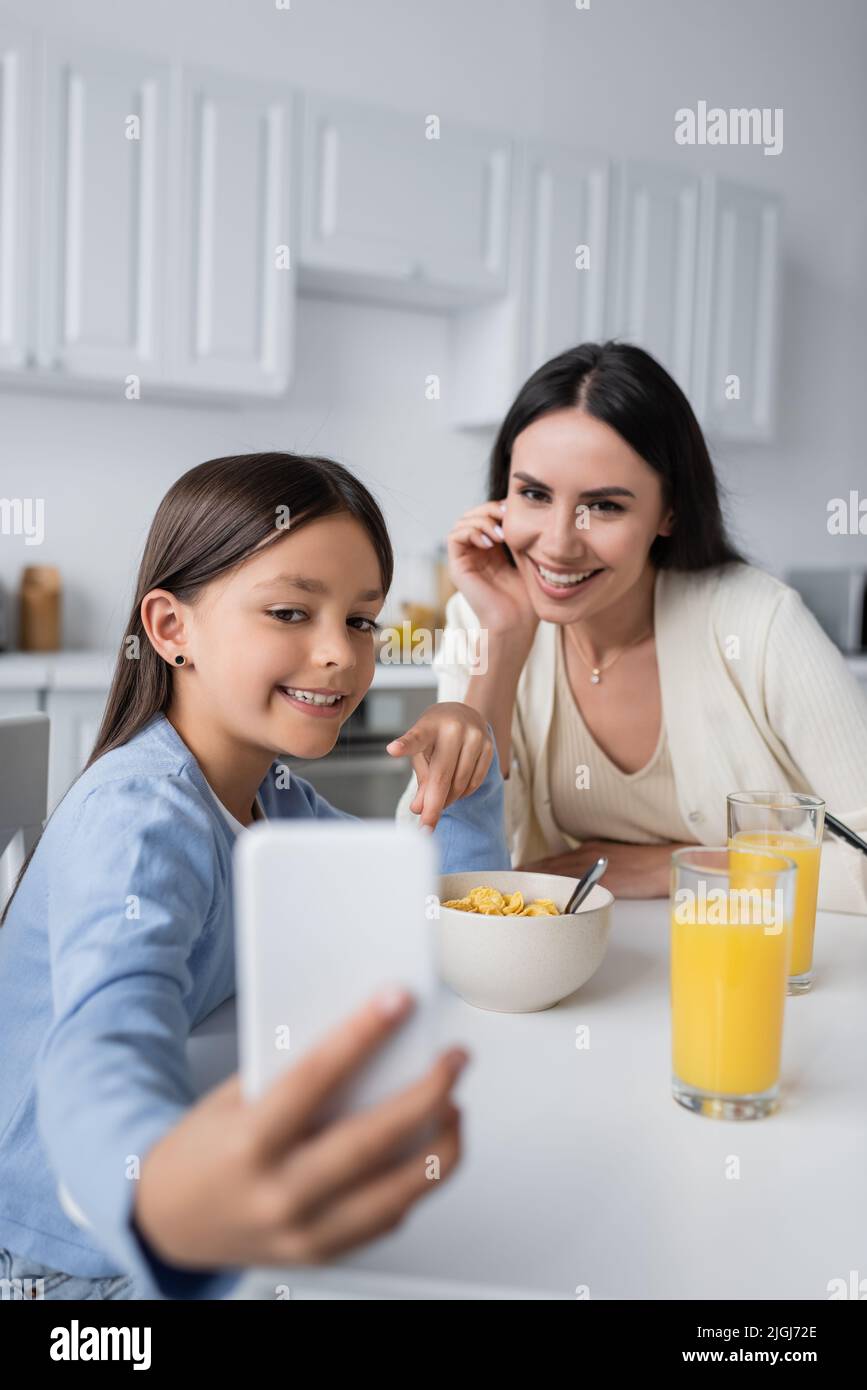 la ragazza felice che mostra il telefono mobile offuscato al babysitter durante la colazione Foto Stock