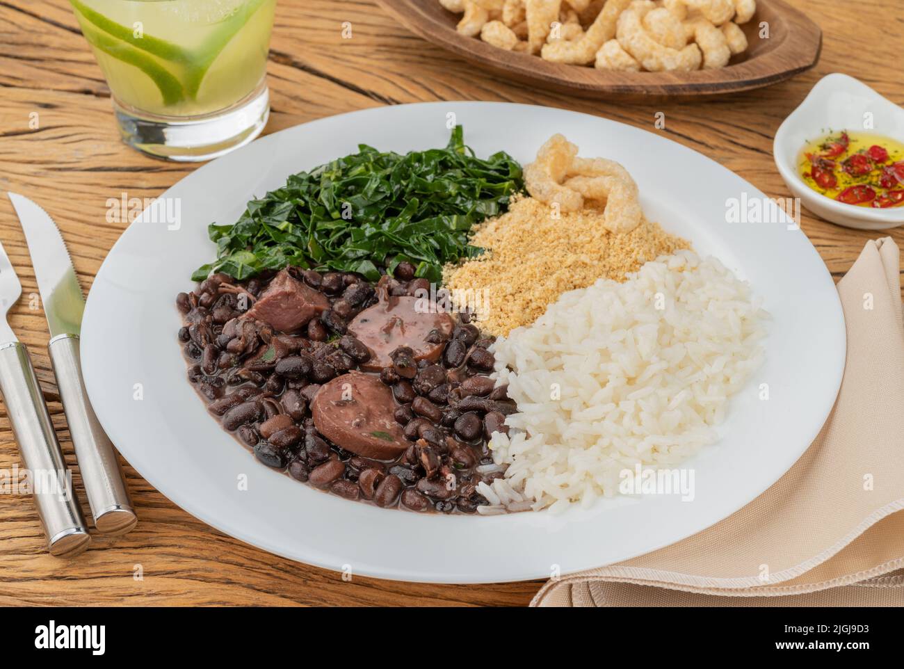 Tipica feijoada brasiliana con riso, pepe, farofa, kale, caipirinha e crackling. Foto Stock