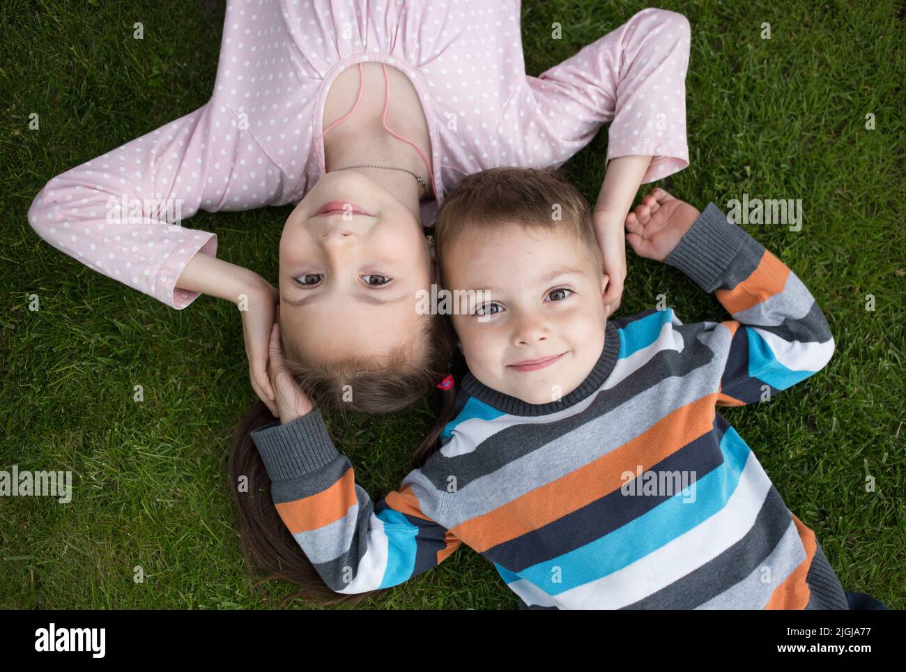 carino sorridente sorella maggiore di 7 anni e fratello minore di 3 anni si trovano fianco a fianco sull'erba, guardare in su. concetto di infanzia felice, amichevole dieci Foto Stock