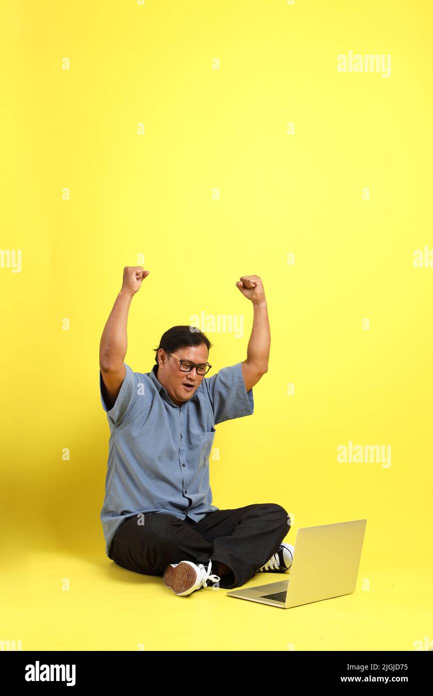 L'uomo asiatico adulto con camicia blu seduta su sfondo giallo. Foto Stock