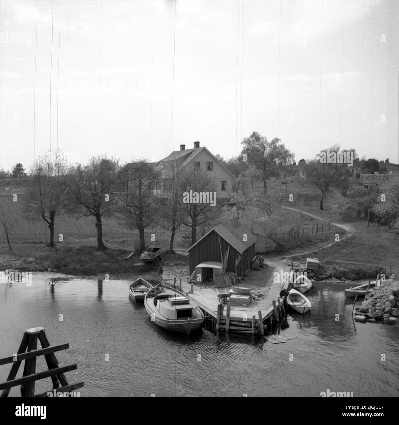 Tilläggsplats Vista verso Västra Skällön dal ponte ovest di Skällösund. La casa di Focus è il fratello Herman e la fattoria di Leonard Pettersson. Sotto un sito aggiuntivo con archi e moli dove vediamo canoe di caccia a destra. A sinistra si vede una manopola, chiamata anche gommone con qualche tipo di quercia davanti ad essa. Al bordo del ponte una boathouse. Foto Stock