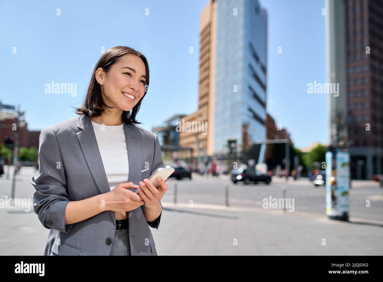 Giovane donna d'affari asiatica sorridente usando il telefono in piedi sulla strada della grande città. Foto Stock