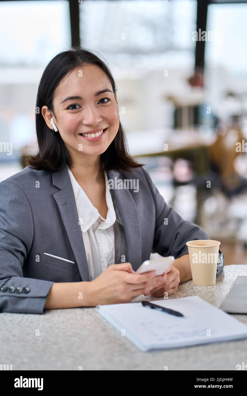 Giovane donna d'affari asiatica felice che indossa un abito con smartphone. Verticale Foto Stock