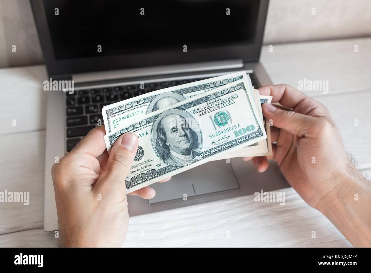 Uomo che detiene cento dollari bollette sopra il laptop Foto Stock