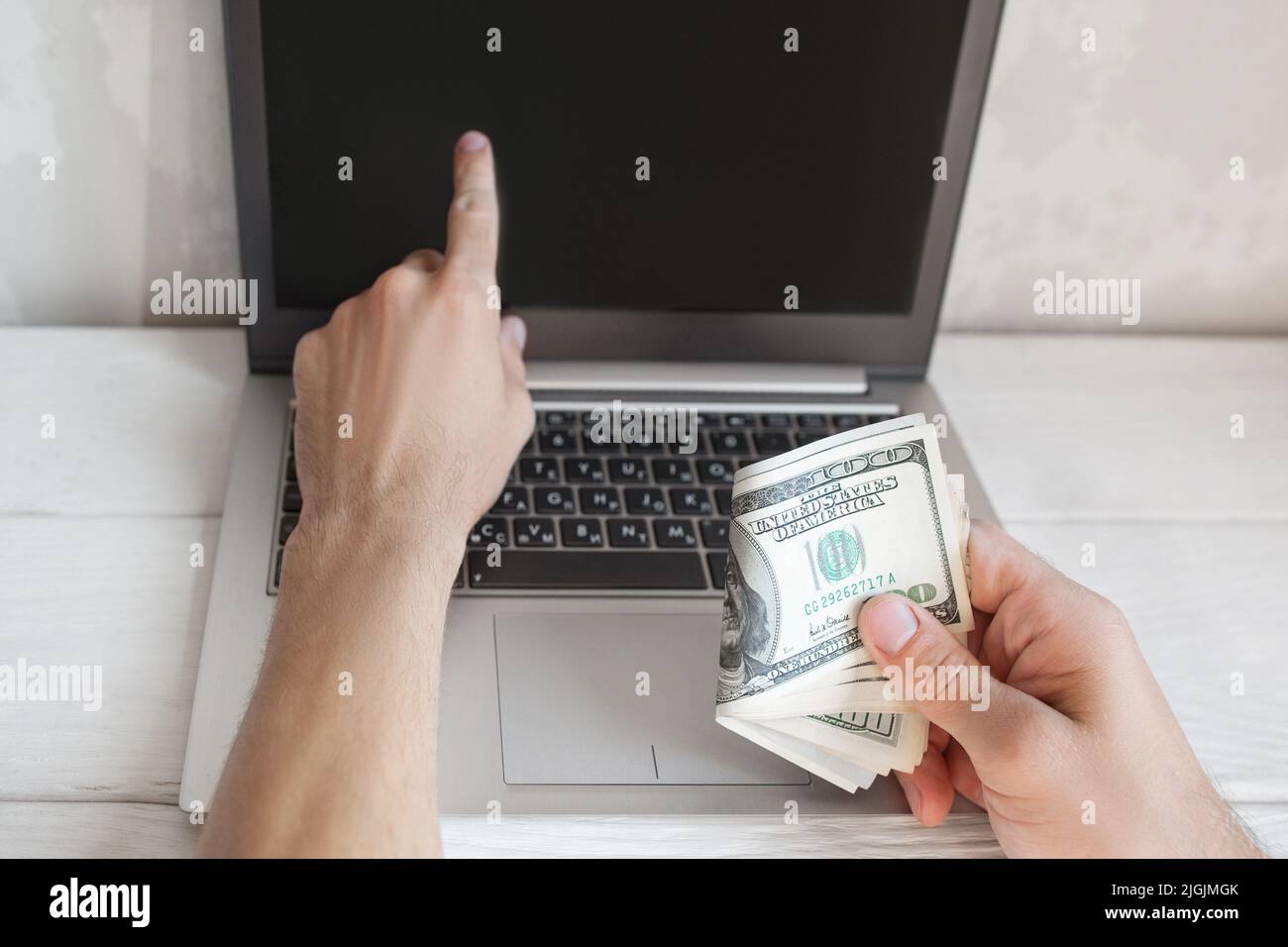 Man punta allo schermo del laptop con i dollari in mano Foto Stock
