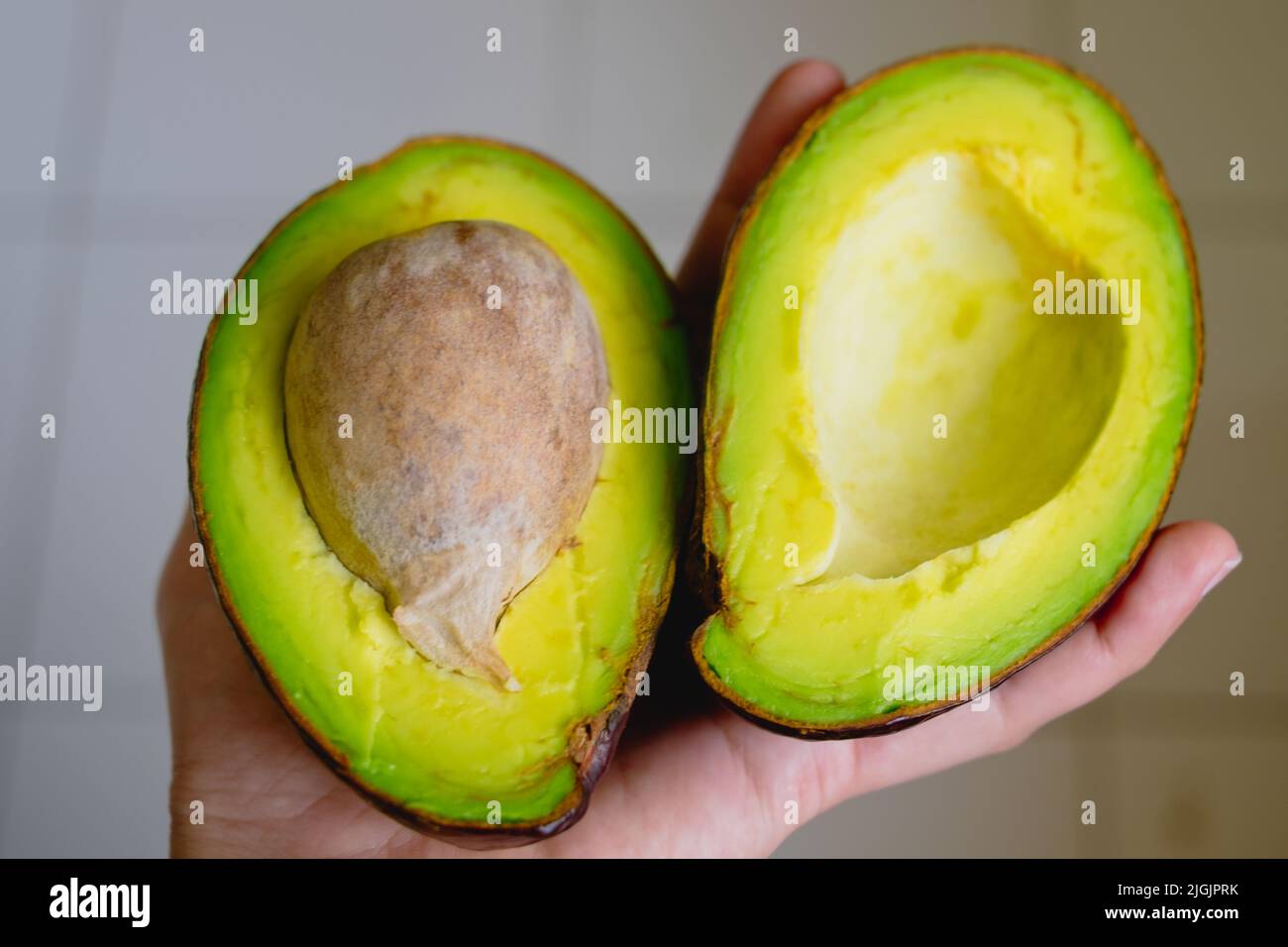 Primo piano della mano sinistra che tiene due fette di avocado biologico appena raccolto super cibo maturo. Messa a fuoco selettiva. Foto Stock