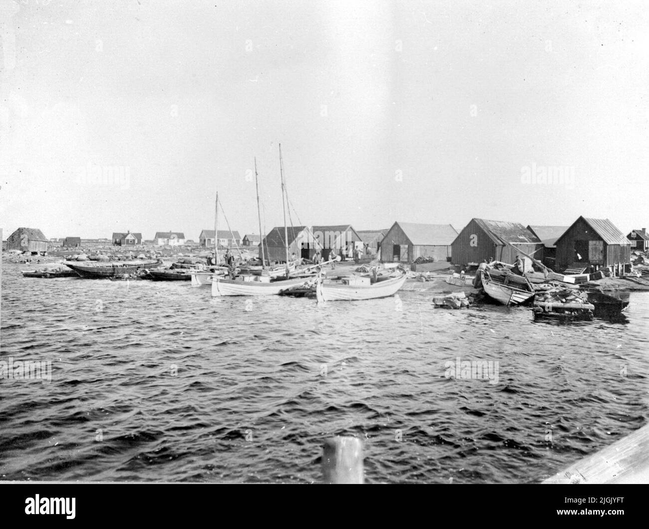 Hamn Boathouses / cabine di pesca nel porto di Stenshamn e barche da pesca come patatine, decori sbiancanti e altri. Sullo sfondo edifici residenziali. Foto Stock