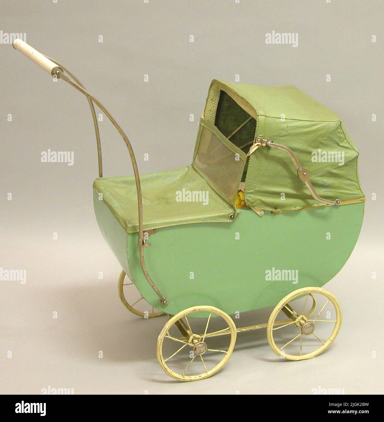 Dockvagn Carrello bambola verde con lati di masonite. Fondo in legno. Montato su supporto in acciaio verniciato bianco. Ruote con pneumatici in gomma. Gomma deformata a causa dell'età. La maniglia obliquamente. In tessuto scamosciato pieghevole. Il suflet coperto di panno verde oliato. Parabrezza e pioggia removibili in tessuto verde oliato con "finestre in plastica" pieghevoli. Timbro sul lato inferiore Emmaljunga. Inger-Maj nacque nel 1944 e ottenne la bambola con il carro quando aveva 4-5 anni. Poi risiede su Saltö. Dono 2005-12-14 da Inger-Maj Gustavsson, Karlskrona Foto Stock