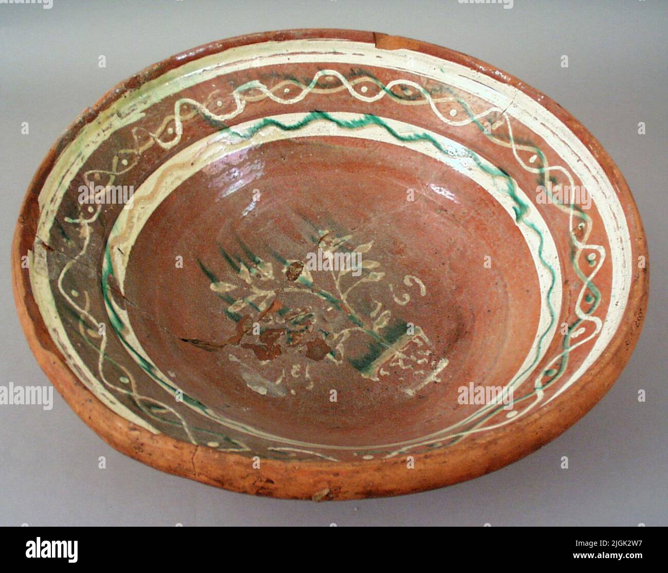 Piatto di argilla grassa di argilla di terracotta rossa, smaltato internamente con glassa trasparente. Decorate con engobe verde e bianco. In fondo datato 1869 e fiori in vaso. Lesioni lungo il bordo e sul fondo così come una spaccatura costante. Foto Stock