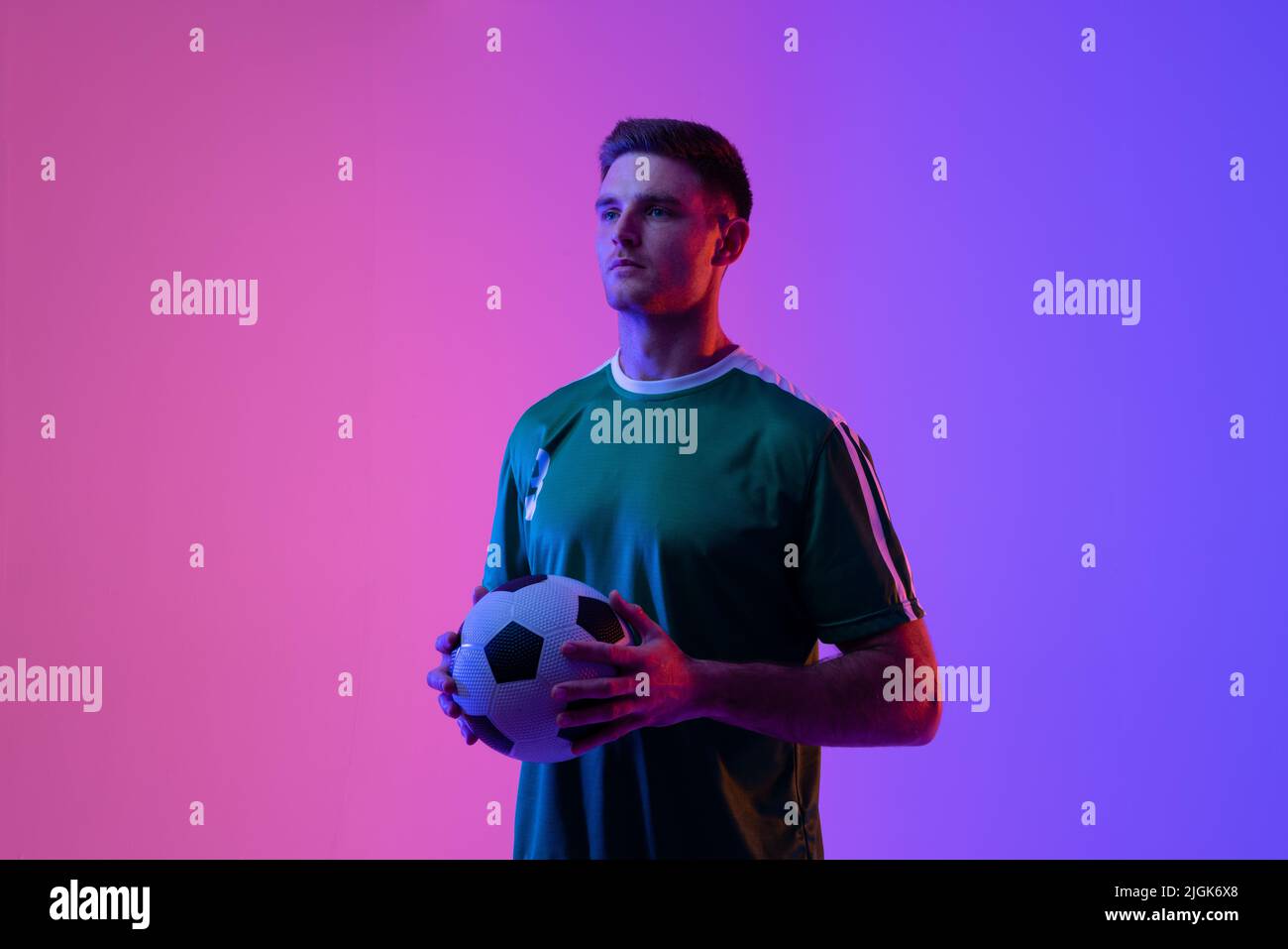 Giocatore di calcio maschile caucasico con football su luci neon rosa Foto Stock