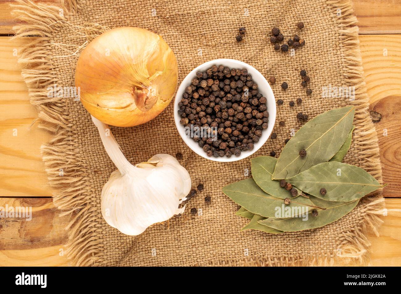 Pepe nero fragrante secco, foglia di alloro, cipolla e aglio con un tovagliolo di iuta su un tavolo di legno, primo piano, vista dall'alto. Foto Stock