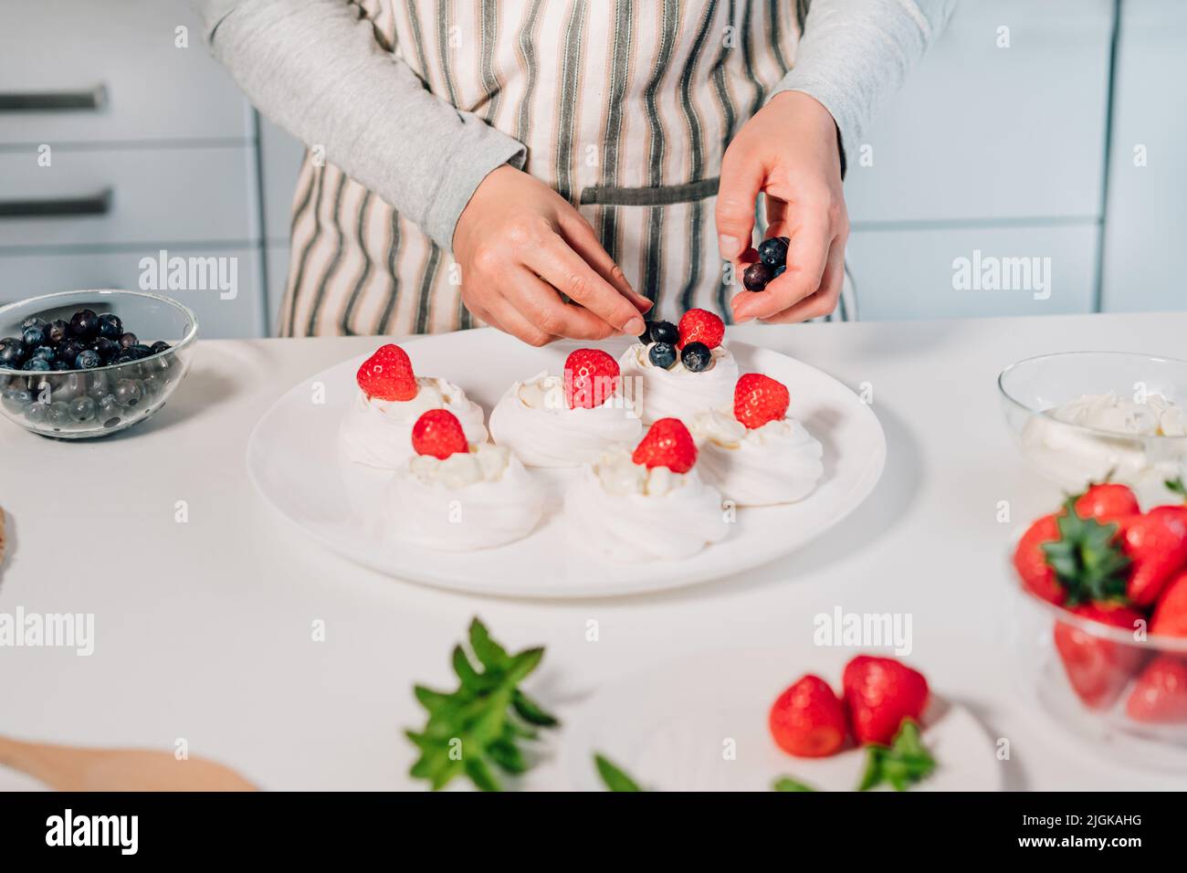 Cucina, facendo meringa fatta in casa. Donne mani che decorano torte Pavlova con frutti di bosco freschi sul tavolo da cucina con ingredienti. Ricette per delicio Foto Stock