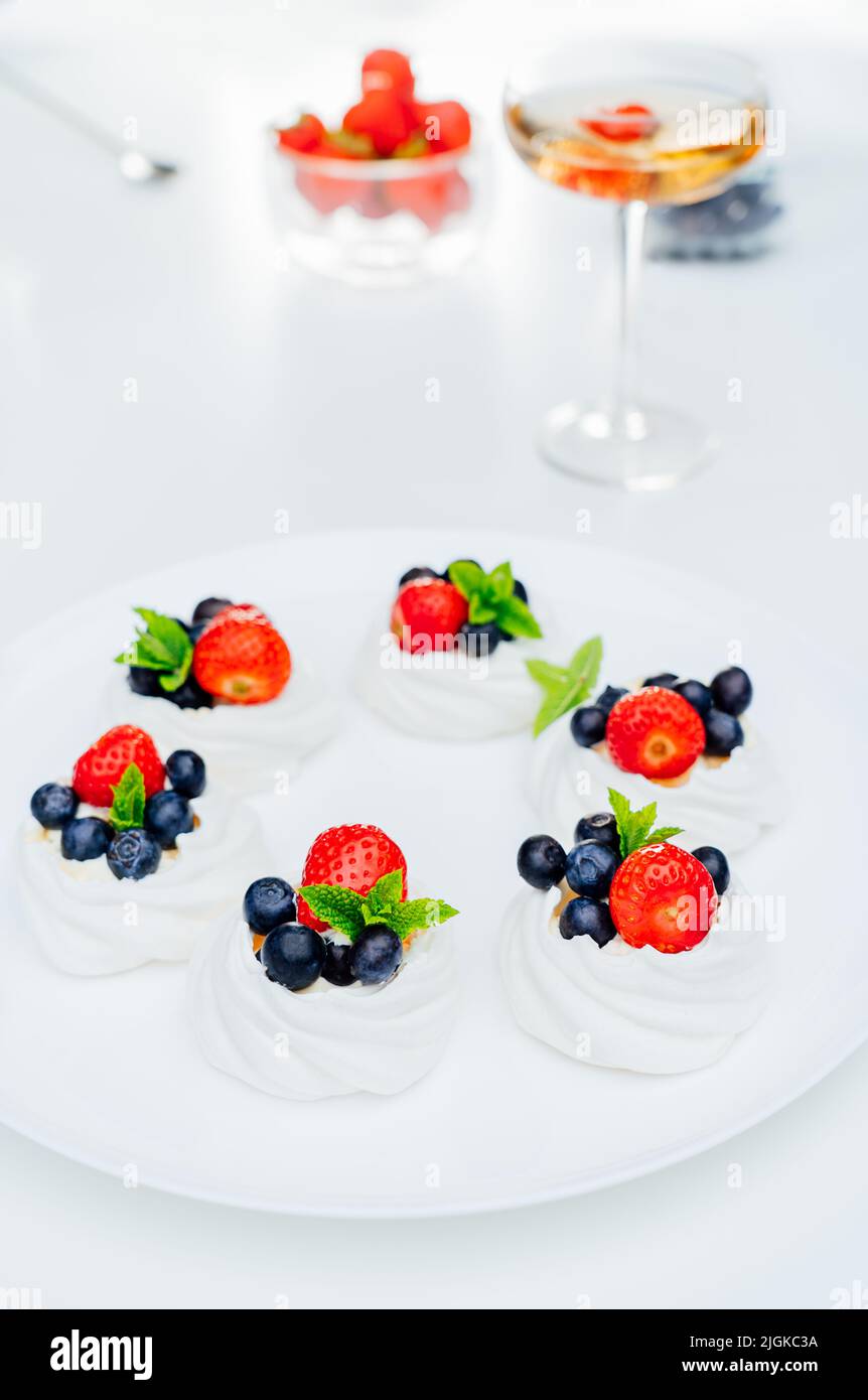 Primo piano torta meringa Pavlova con fragole fresche e mirtilli con menta sul piatto bianco e cocktail con fragola. Dessert e. Foto Stock