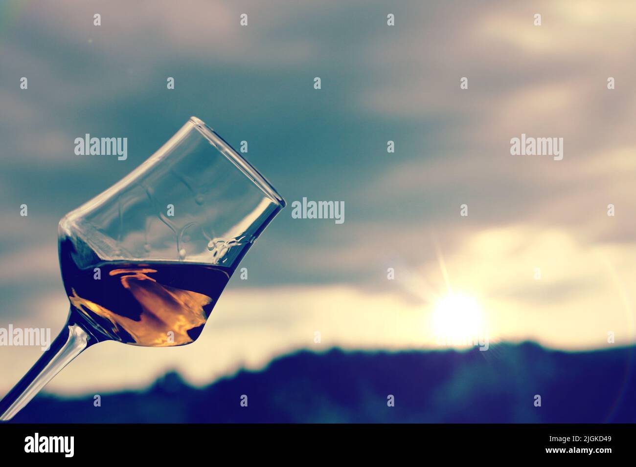 Bicchiere di vino dolce con un giardino al tramonto toscano come sfondo. Foto Stock