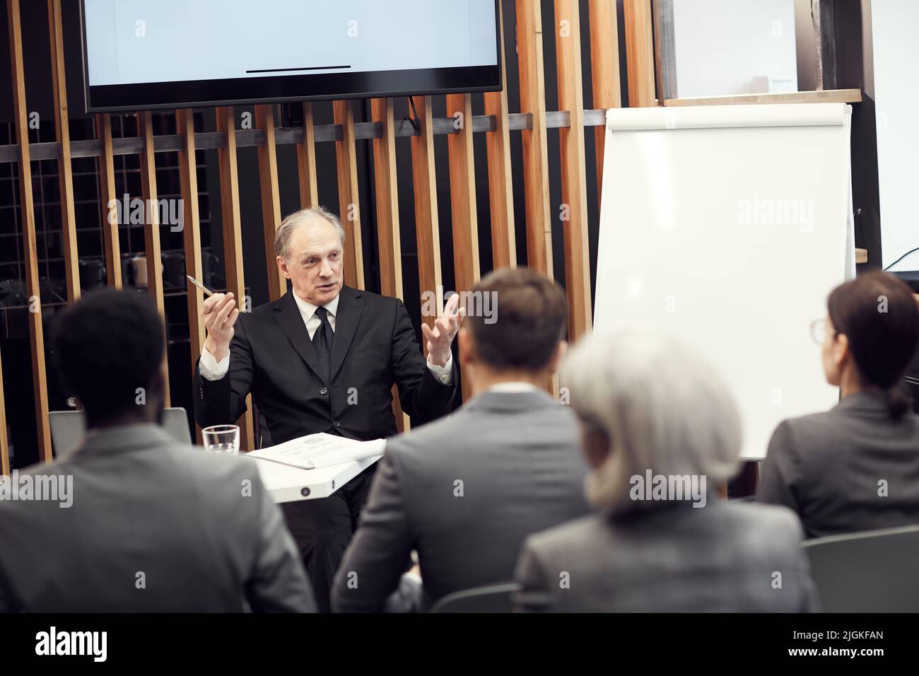 Emotivo Senior maschio proprietario della società seduto al tavolo con appunti e gesturing mani mentre si parla espressivamente a riunione Foto Stock