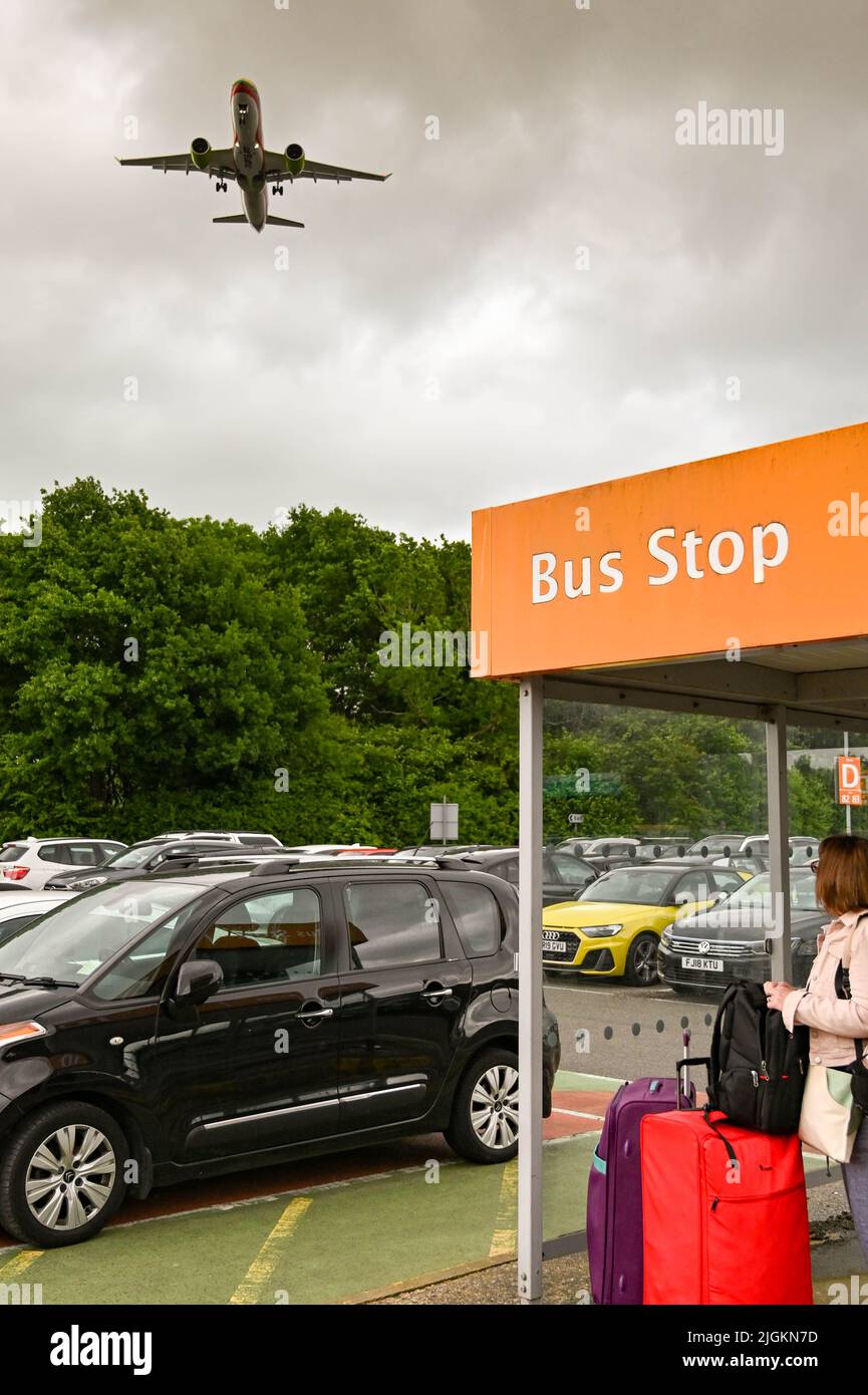 Londra, Inghilterra - Giugno 2022: Persona in attesa a una fermata dell'autobus in uno dei parcheggi per soggiorni prolungati all'aeroporto di Gatwick. Un aereo vola in alto. Foto Stock