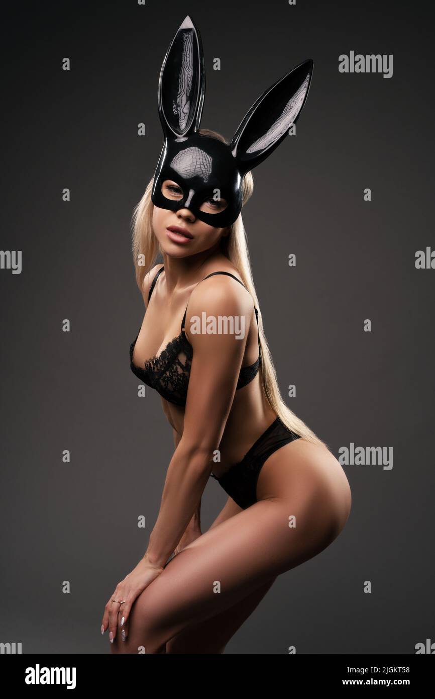Giovane donna sexy in intimo e maschera di coniglio in piedi in nero studio Foto Stock